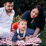 A joyful family enjoying a picnic outdoors during summer. Smiling parents with their baby on a blanket.