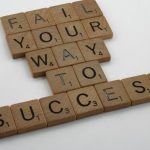 Wooden tiles spell 'Fail Your Way to Success' emphasizing perseverance.